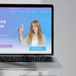 Laptop prezentuje stronę z blondynką trzymającą probówkę, wzór chemiczny i napisy. Niebiesko-fioletowe tło, nowoczesny design. Domena paolaproject.pl.