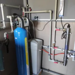 Kompleksowa instalacja uzdatniania wody z filtrem Multitower S, sterylizatorem UV i zbiornikiem. Rury z zaworami zamocowane do ściany. Realizacja w pomieszczeniu z płytkami.