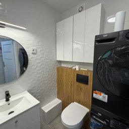 REN Bud - Nowoczesna łazienka po remoncie: białe płytki 3D, szafki wiszące, umywalka z lustrem, toaleta i pralko-suszarka Beko w czarnym kolorze. Widoczne detale wykończenia.