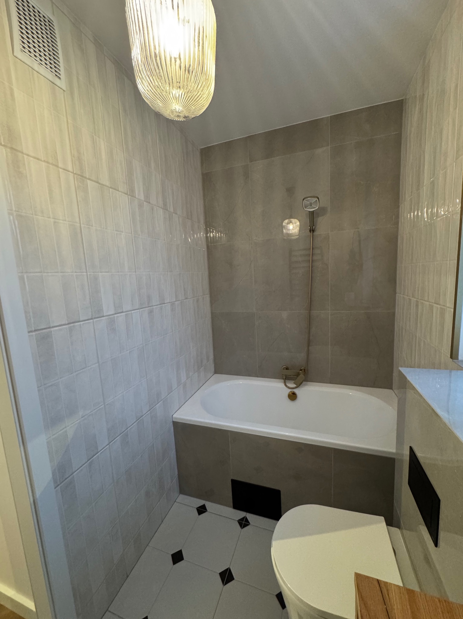 Wykończona łazienka w Szczecinie: biała wanna, toaleta i szare płytki na ścianach. Uwagę przykuwa designerska lampa sufitowa.