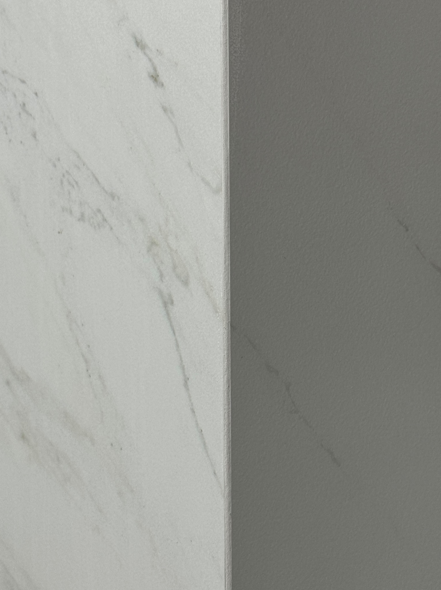 Połączenie dwóch powierzchni: biała marmurowa płytka i szara ściana. Widoczny narożnik, oświetlenie równomierne, minimalistyczny kadr.