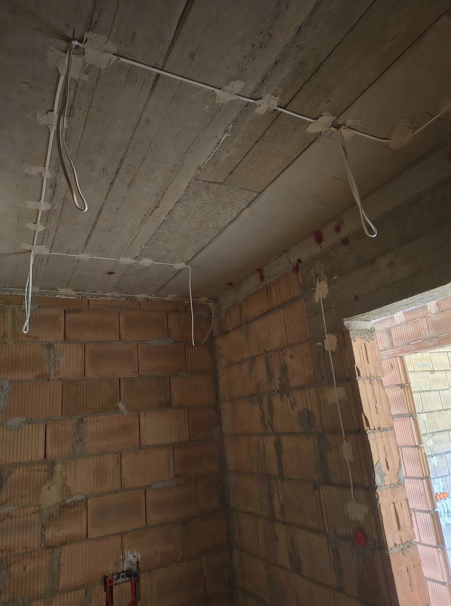 Wewnętrzne kable elektryczne przymocowane do surowego betonowego sufitu i ceglanych ścian w trakcie budowy. Widoczne elementy instalacji.