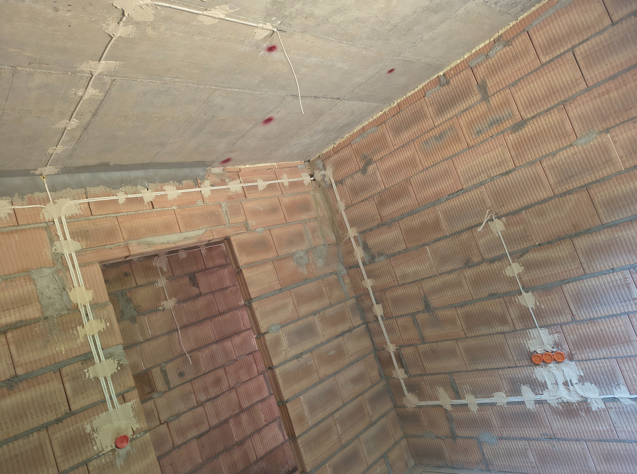 Surowy stan: instalacja elektryczna natynkowa w nowym budynku z czerwonej cegły, widoczne kable i puszki. Oznaczenia na suficie.