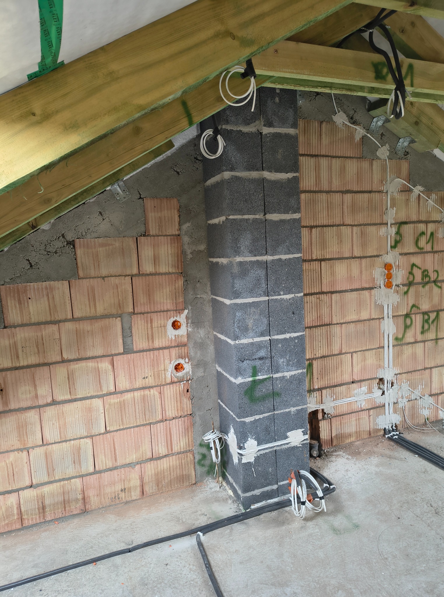 Surowy stan poddasza z instalacją elektryczną w ścianach z cegły dziurawki i pustaków szarych, widoczne kable i puszki elektryczne, drewniana konstrukcja dachu.