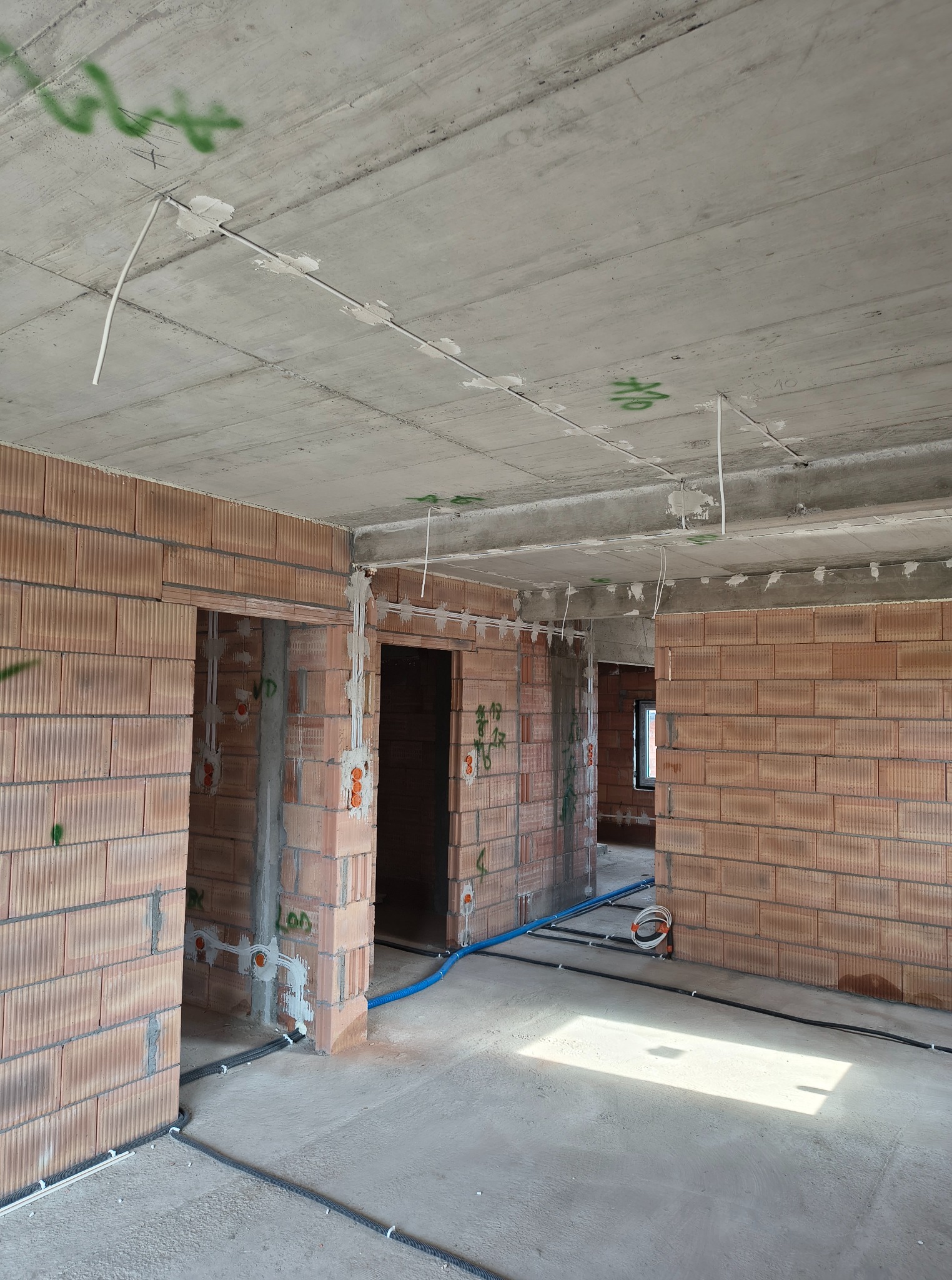 Wnętrze w trakcie prac, widoczne kable elektryczne prowadzone po ścianach i suficie, oraz rury w podłodze. Ściany z czerwonej cegły, surowy betonowy sufit.