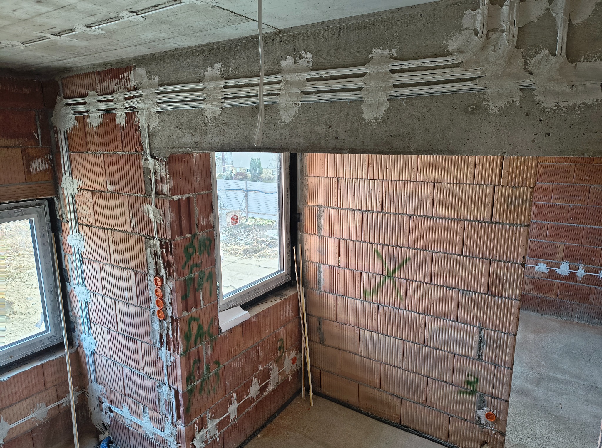 Wewnętrzne ściany z pustaków z instalacją elektryczną w peszlach, częściowo zamurowane. Widoczne puszki elektryczne i przewody. Surowy stan wykończenia.