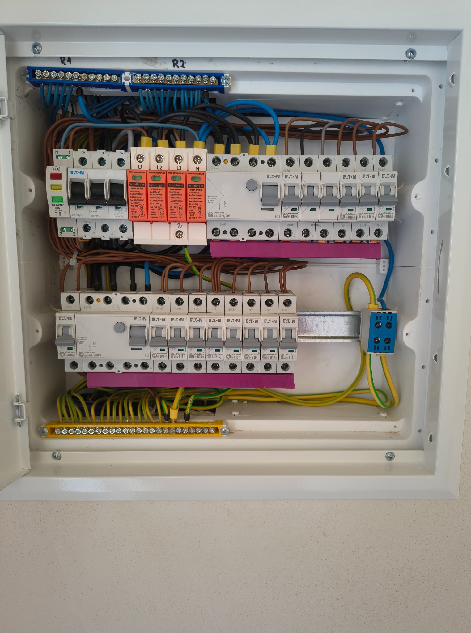 Rozdzielnica elektryczna w białej obudowie, widoczne bezpieczniki, przewody w różnych kolorach, listwy zaciskowe i oznaczenia.