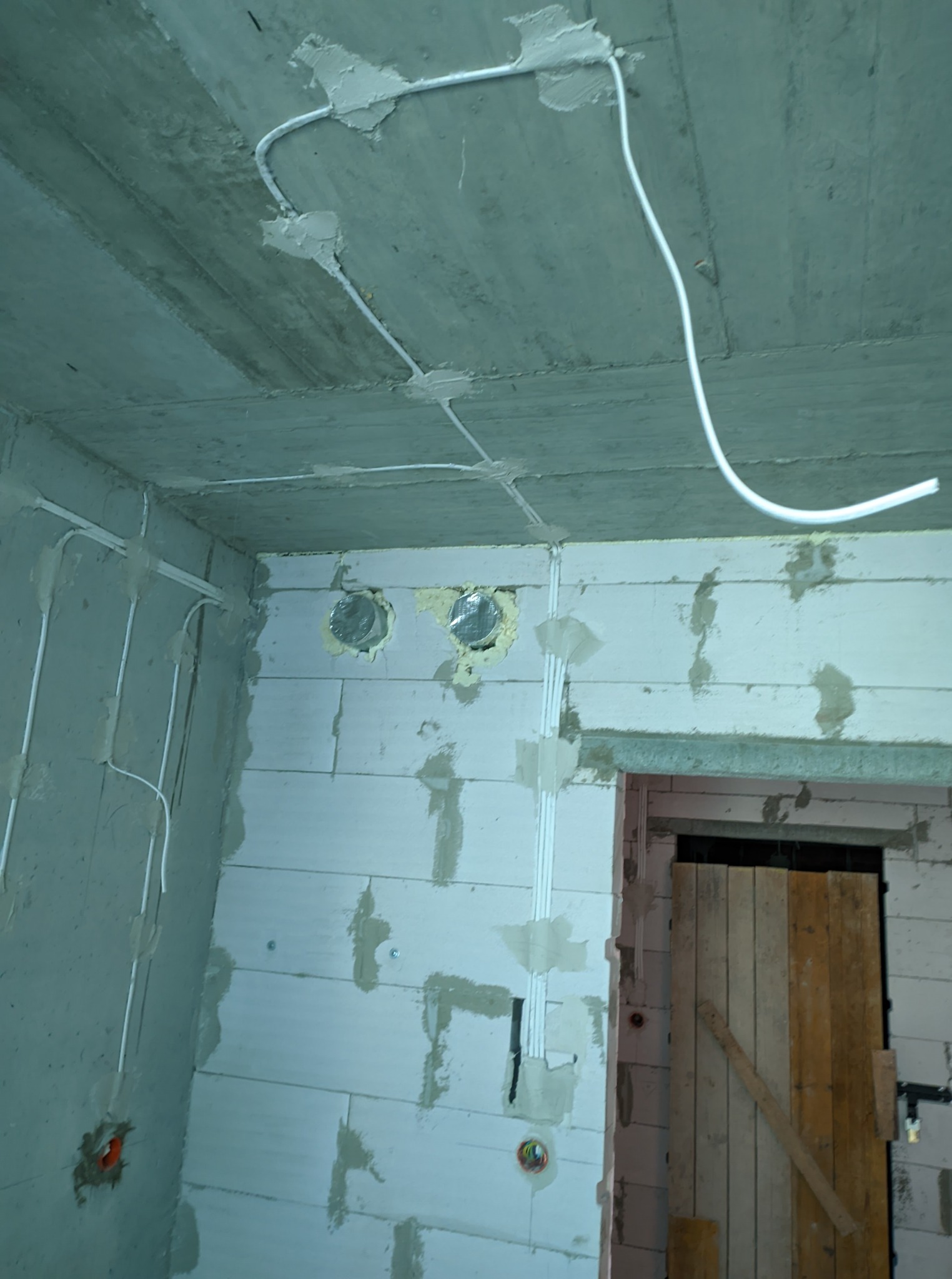 Białe przewody elektryczne przymocowane do surowego betonowego sufitu i ścian z betonu komórkowego w trakcie instalacji, widoczne puszki instalacyjne.
