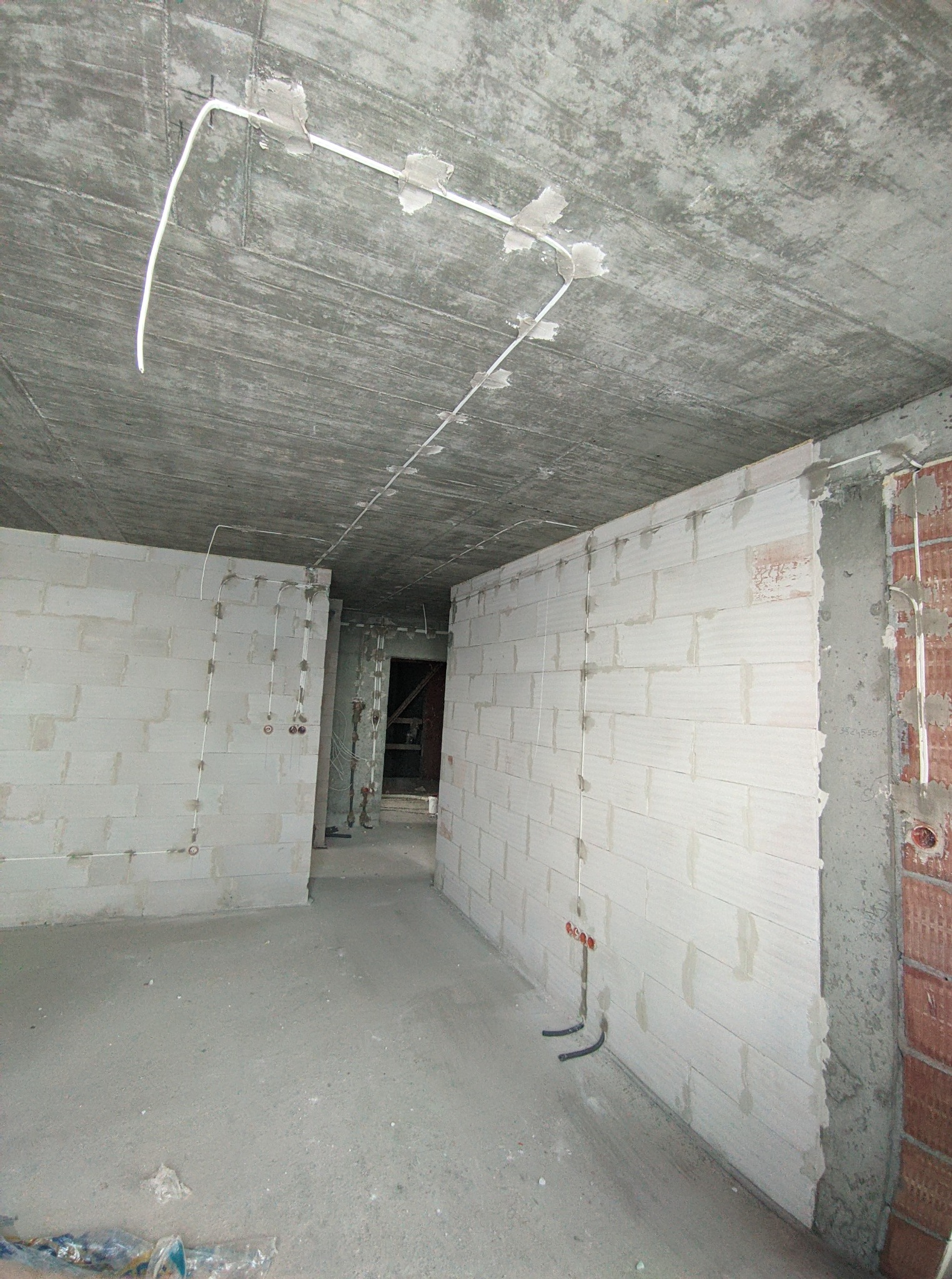 Surowy stan mieszkania z widoczną instalacją elektryczną: kable prowadzone po suficie i ścianach, puszki elektryczne w ścianach z betonu komórkowego.