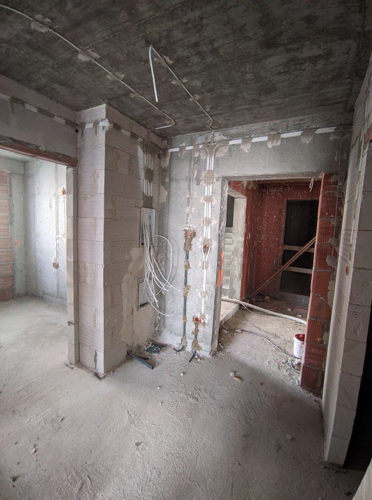 Wnętrze w stanie surowym, widoczne ściany z bloczków, instalacja elektryczna w peszlach, puszki podtynkowe i przewody. Stan prac przed tynkowaniem.