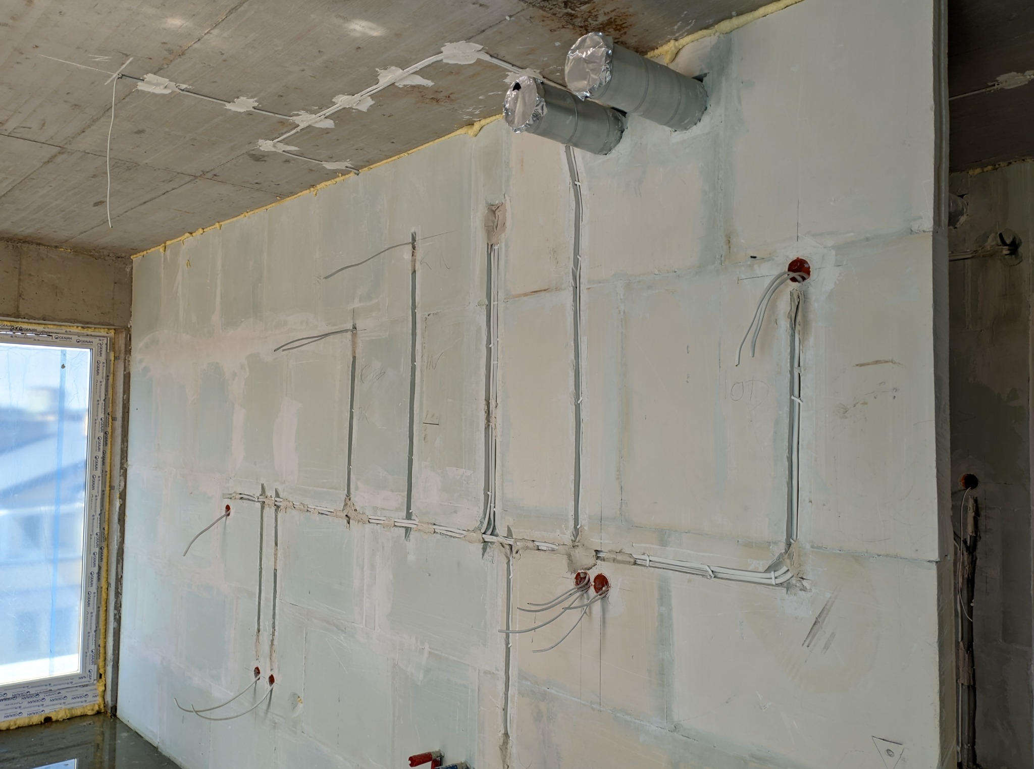 Instalacja elektryczna w surowym wnętrzu: kable w ścianach z gipsu, puszki elektryczne, wentylacja. Etap prac przed wykończeniem, widok na okno.
