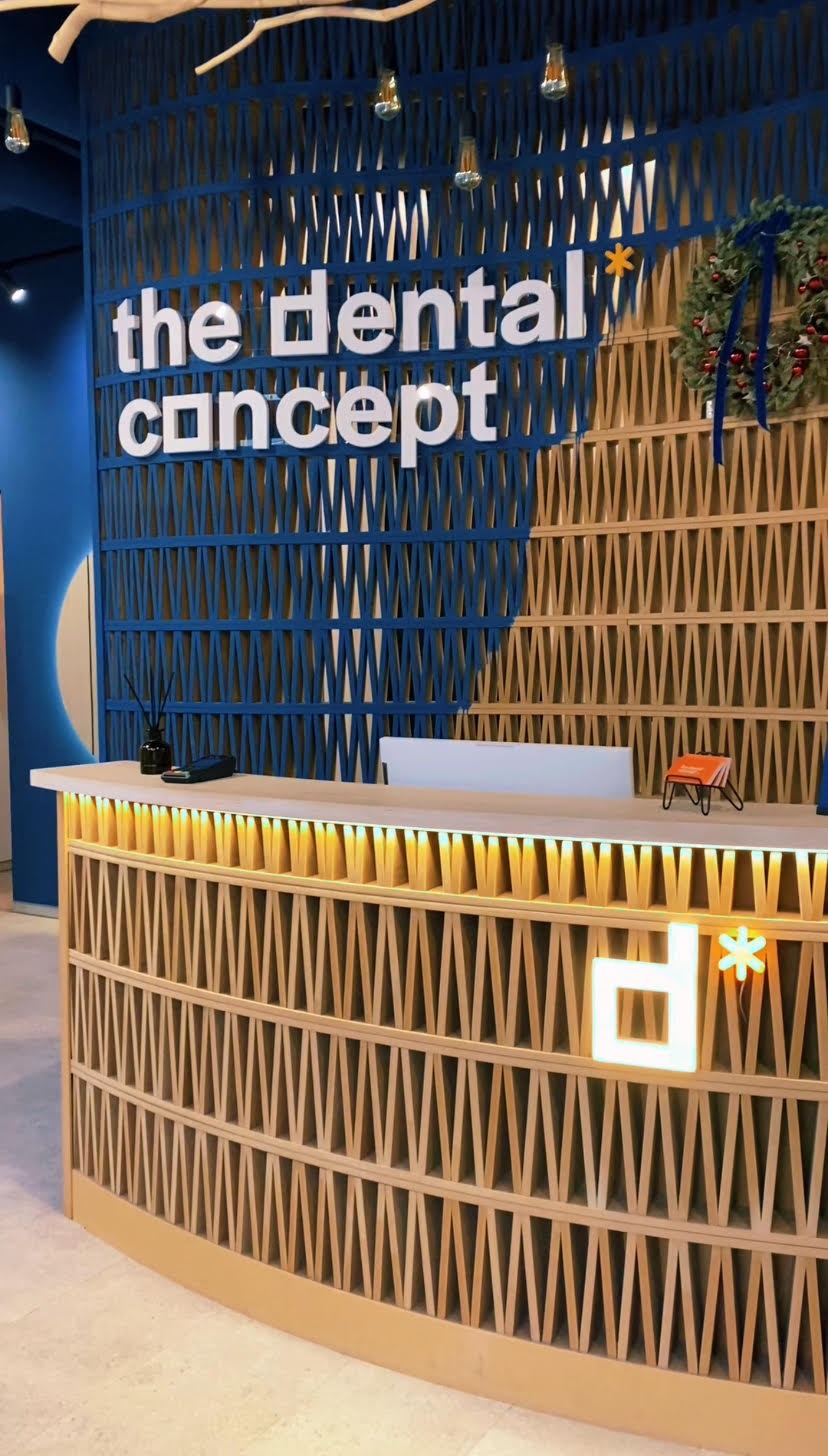Recepcja gabinetu stomatologicznego z drewnianą ażurową ścianą w kolorze niebieskim i beżowym, podświetlonym logo i świątecznym wieńcem.