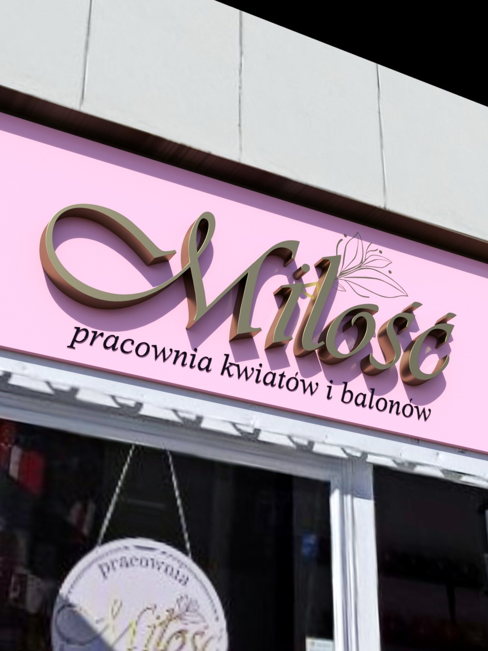 Złoty napis 'Miłość pracownia kwiatów i balonów' na różowym tle nad wejściem do lokalu. Widoczny fragment drzwi z tabliczką pracowni.