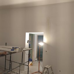 BEC-BUD FIRMA USŁUGOWO-HANDLOWA KAROL ZAGDAN - Białe ściany po szpachlowaniu, widoczne rusztowanie, lampa halogenowa i drabina. Przygotowania do malowania w trakcie remontu mieszkania.