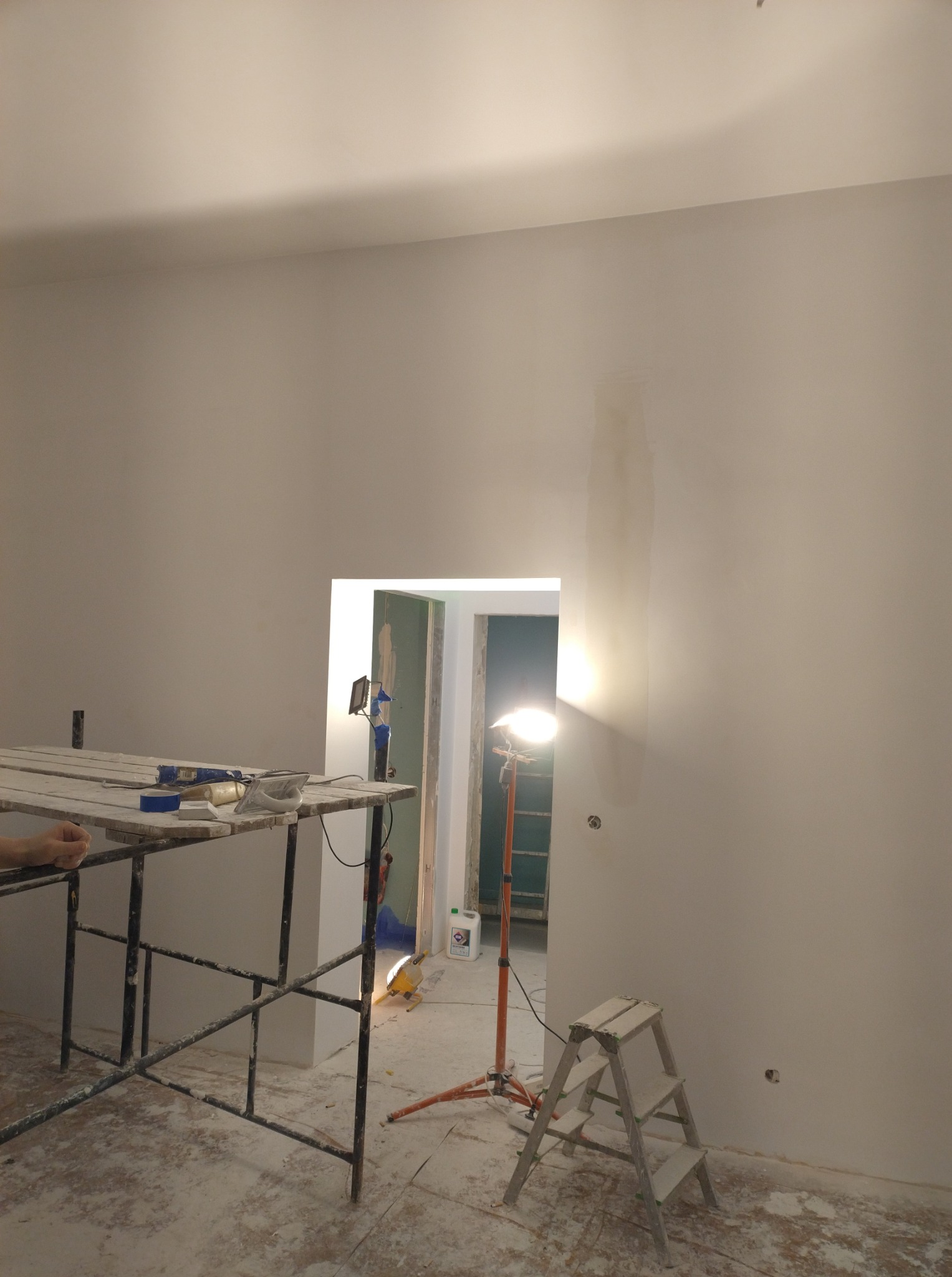 Białe ściany po szpachlowaniu, widoczne rusztowanie, lampa halogenowa i drabina. Przygotowania do malowania w trakcie remontu mieszkania.
