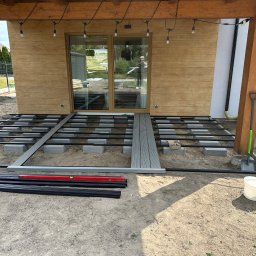 Michał Kowaliński - Montaż tarasu kompozytowego: widok na przygotowany stelaż z belek i bloczków betonowych, z częściowo ułożonymi deskami. Widoczne narzędzia i materiały budowlane.