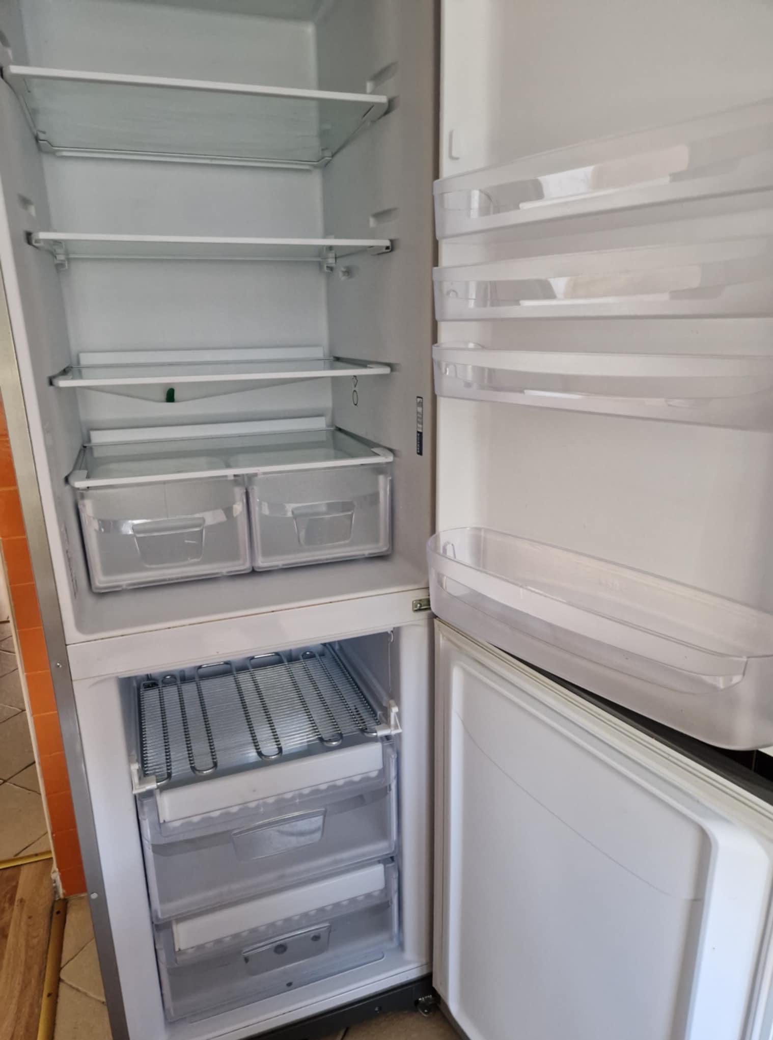 Pusta, otwarta lodówka z półkami i szufladami, gotowa do napełnienia produktami. Widoczne wnętrze urządzenia z metalowymi elementami chłodzącymi.