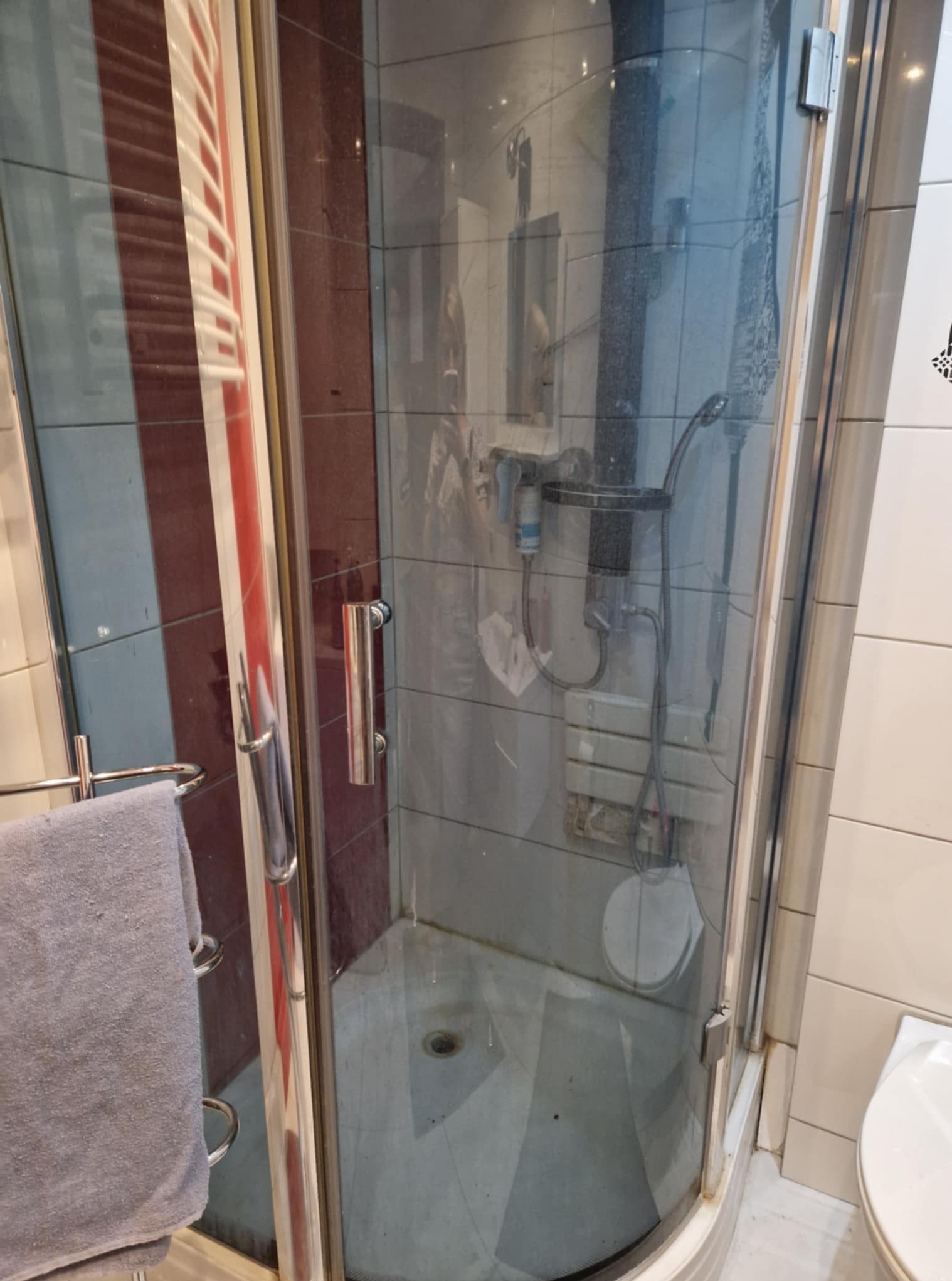 Brudna kabina prysznicowa z osadami na szkle i podłodze. Widoczne ślady po remoncie, niedoczyszczone fugi i ogólny brak higieny.
