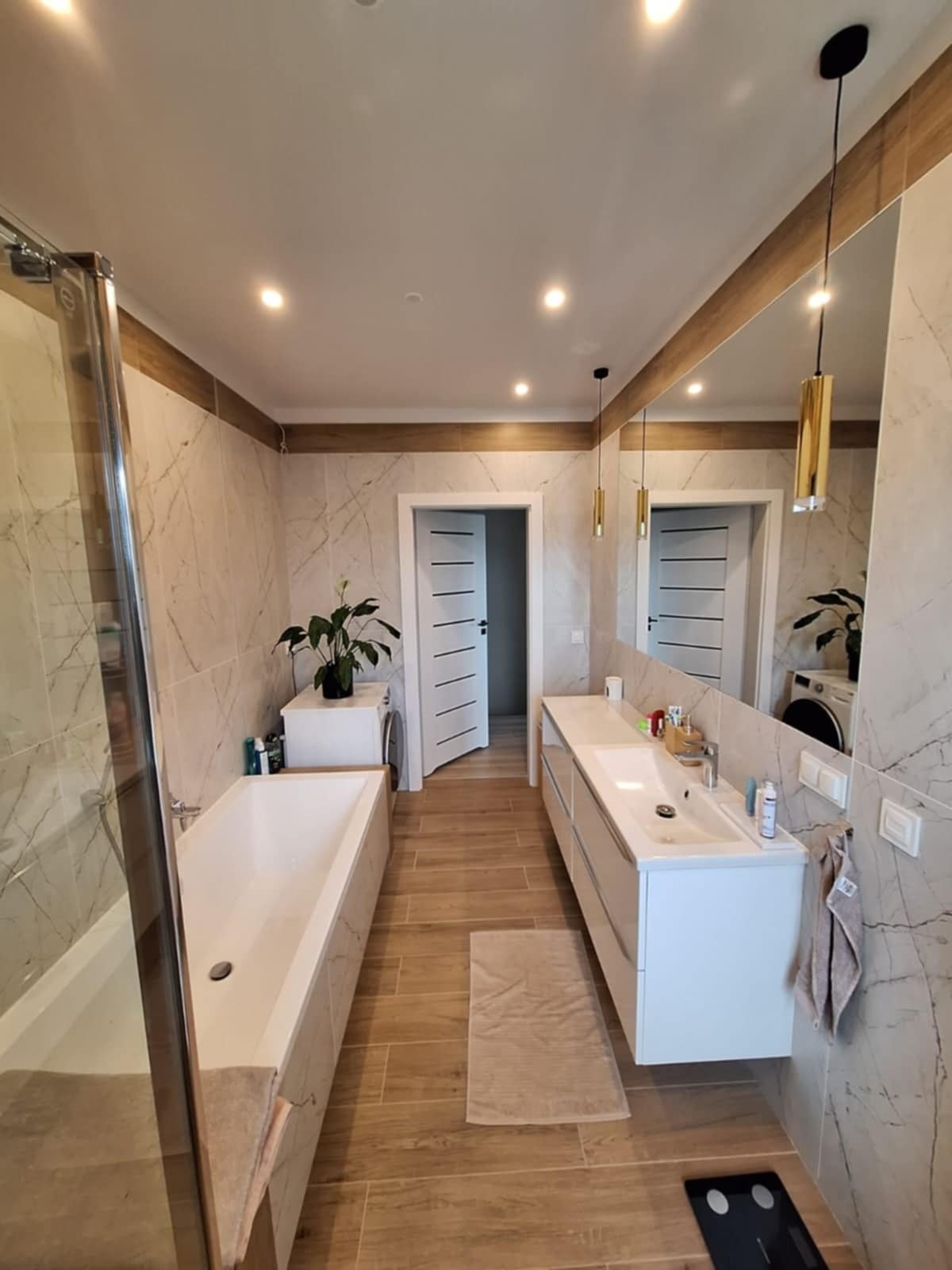 Nowoczesna łazienka z wanną, umywalką i marmurowymi płytkami w Słuszewie. Widoczne oświetlenie punktowe i dekoracyjne lampy wiszące. Minimalistyczny design.