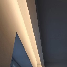 ARTBUD PRO Łukasz Sypnik - Nowoczesne oświetlenie sufitowe LED wnękowe, ciepłe światło podkreśla gładką powierzchnię ściany i sufitu. Widoczny fragment okna i mebli.