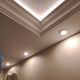 ARTBUD PRO Łukasz Sypnik - Wykończony sufit z oświetleniem LED w listwach i punktowymi lampami. Ściana pomalowana na beżowo, widoczny fragment drabiny malarskiej.