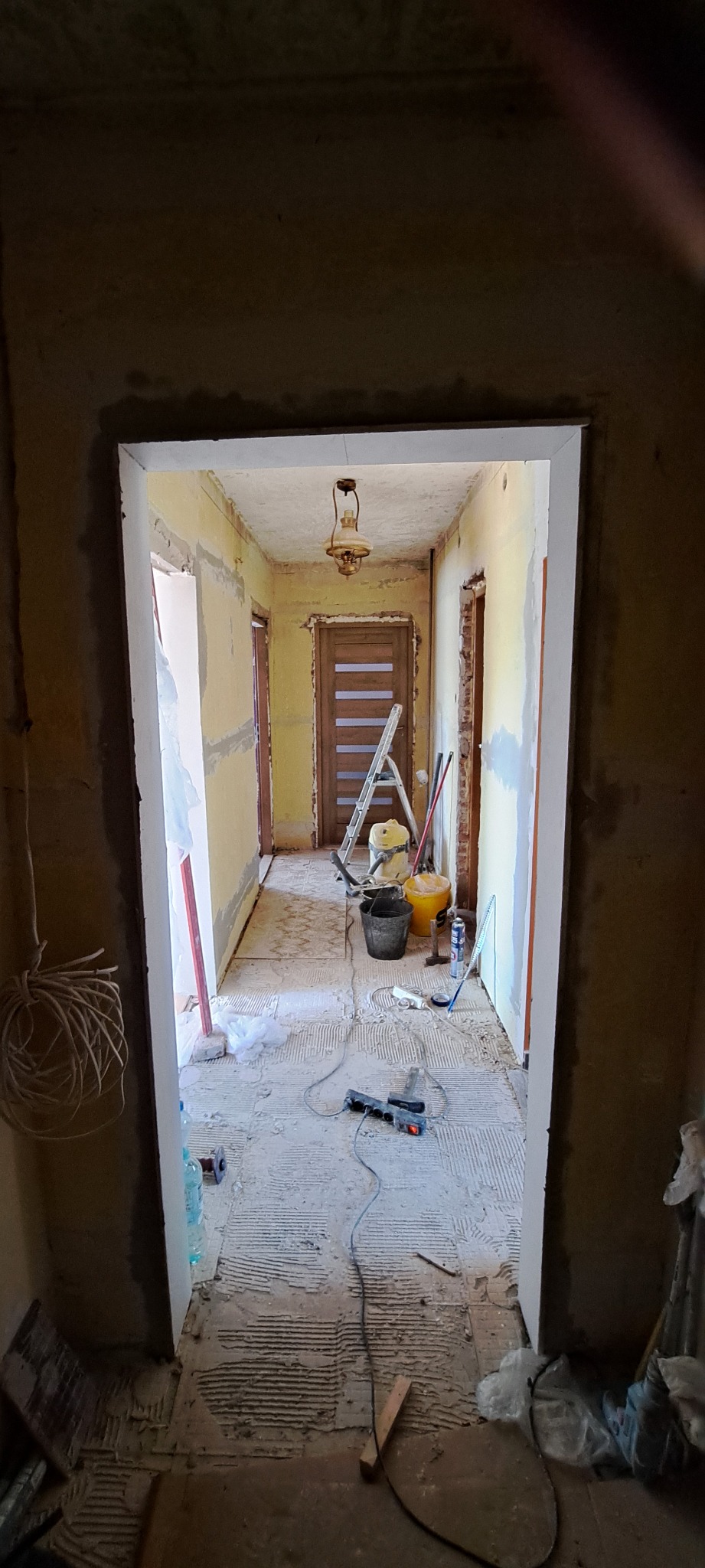 Korytarz w trakcie remontu w Łazach. Widoczne narzędzia, drabina, ściany przygotowane pod malowanie, fragmenty starej instalacji elektrycznej. Etap szpachlowania.