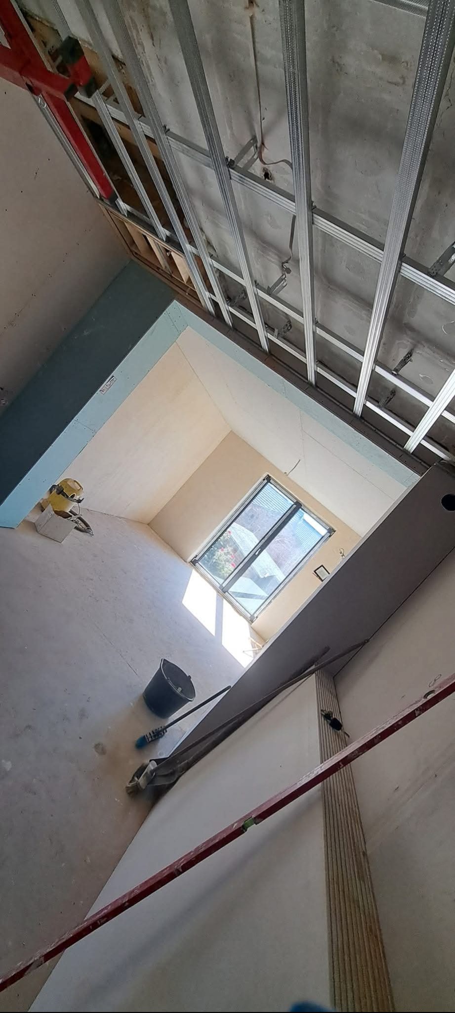 Montaż metalowej konstrukcji sufitu podwieszanego w jasnym pokoju z oknem dachowym. Widoczne narzędzia i materiały budowlane.