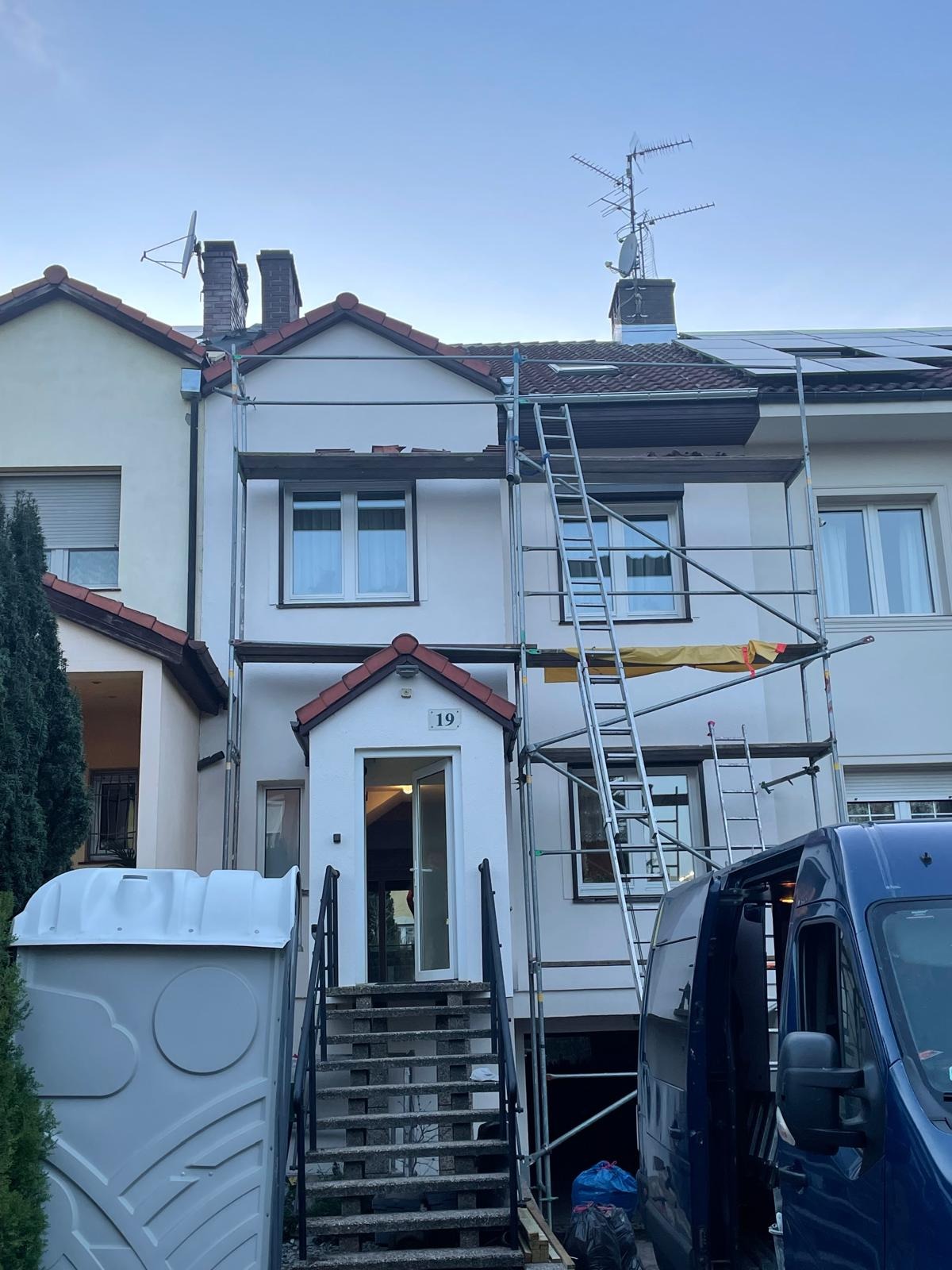 Dom w rusztowaniach przed renowacją elewacji. Widoczny przenośny WC i samochód dostawczy. Dom z numerem 19.