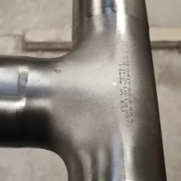 Spoina T ze stali nierdzewnej z kołnierzem, widoczne ślady po obróbce i napisy 'Made in EU'. Precyzyjne połączenia spawane.