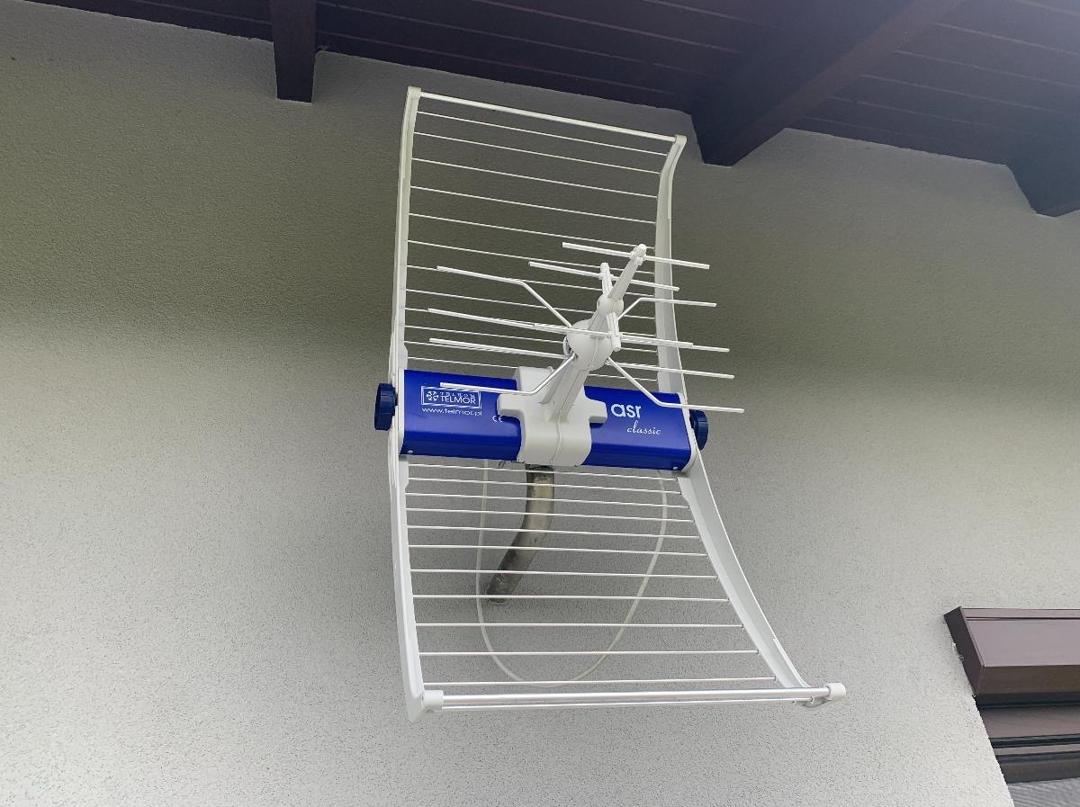 Biała antena telewizyjna typu Yagi-Uda zamontowana na elewacji budynku. Widoczny niebieski element z logo Telmor i napisem 'asr classic'.