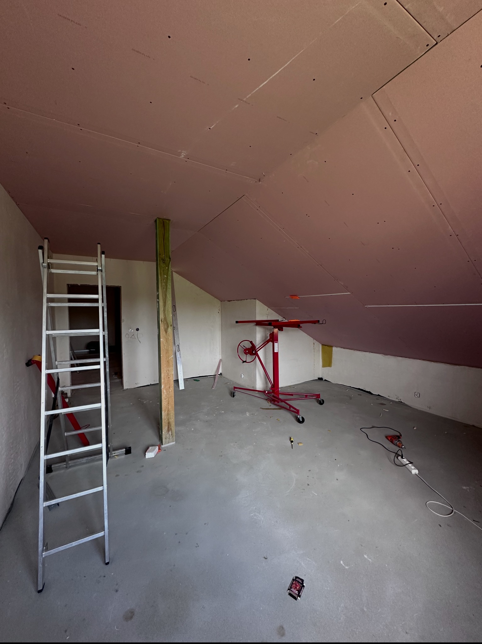 Montaż płyt karton-gips na poddaszu w Łęcznej. Widoczna drabina, podnośnik do płyt i częściowo zamontowane płyty na skosach dachu.