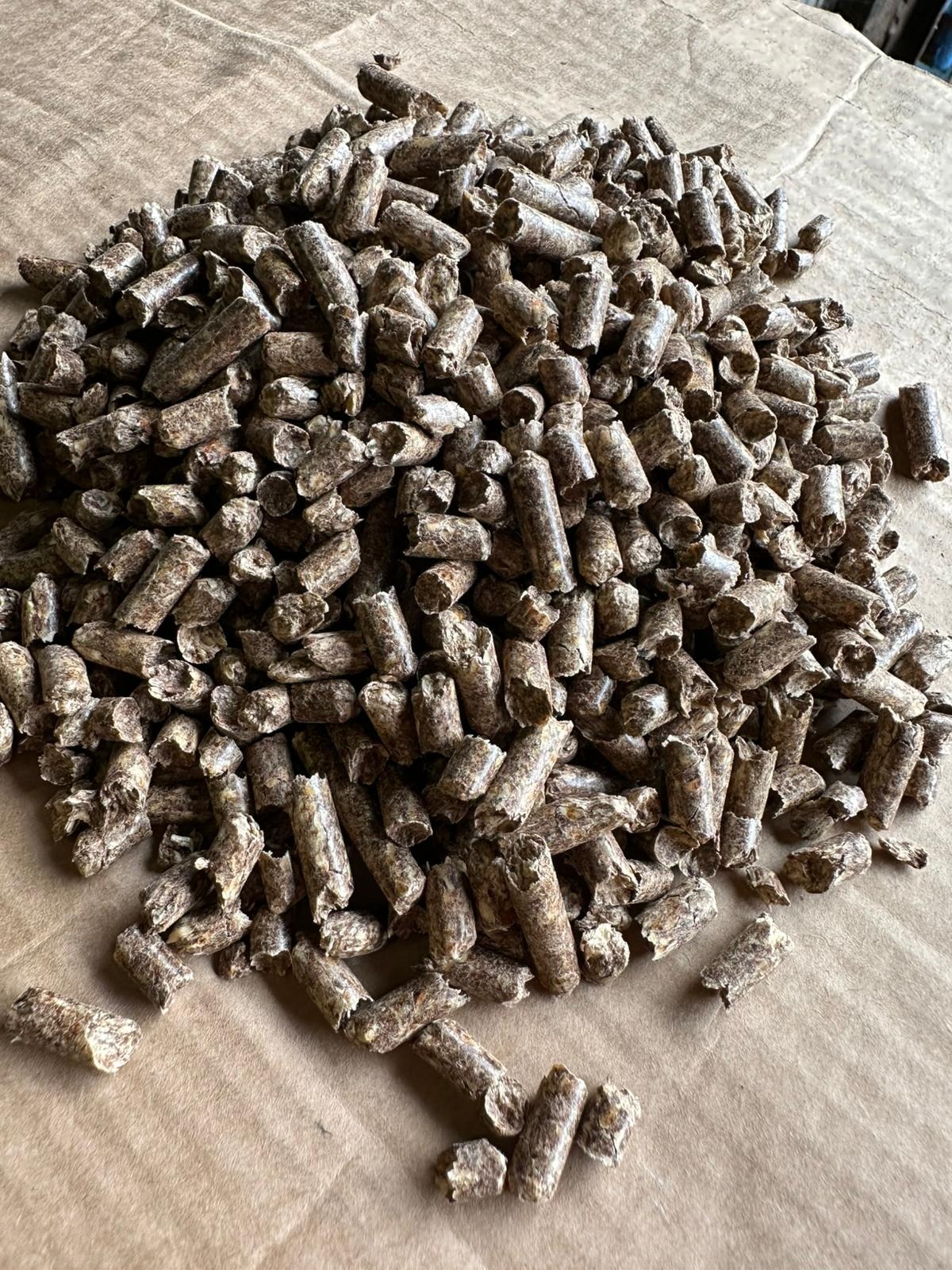 Góra brązowego pelletu drzewnego na szarym tle. Widoczne drobne nierówności i tekstura pelletu. Ujęcie z bliska, ukazujące detale materiału.