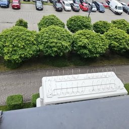 TERMO MOCNI - Biała klimatyzacja z metalowymi zabezpieczeniami na dachu budynku, widok z góry na parking i zieleń.