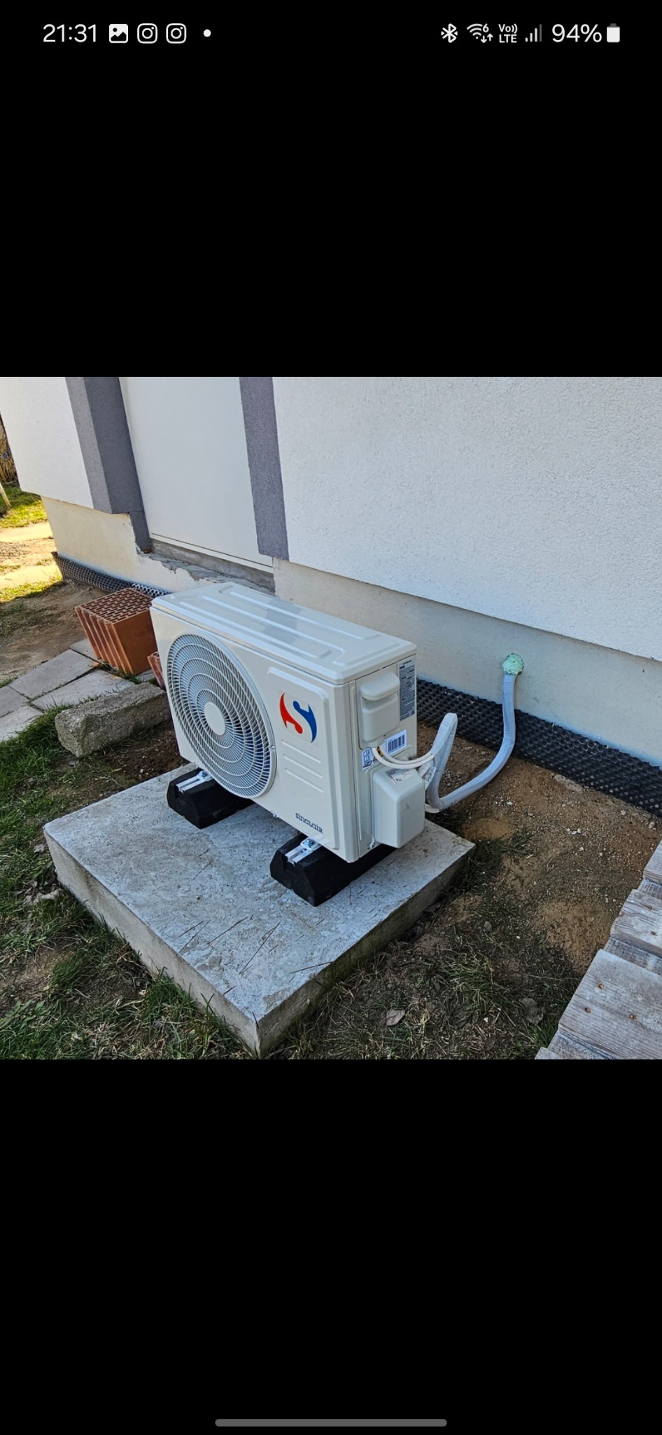 Biała jednostka zewnętrzna klimatyzacji Sinclair na betonowej podstawie, z widocznymi przewodami, zamontowana przy ścianie budynku z szarym cokołem.