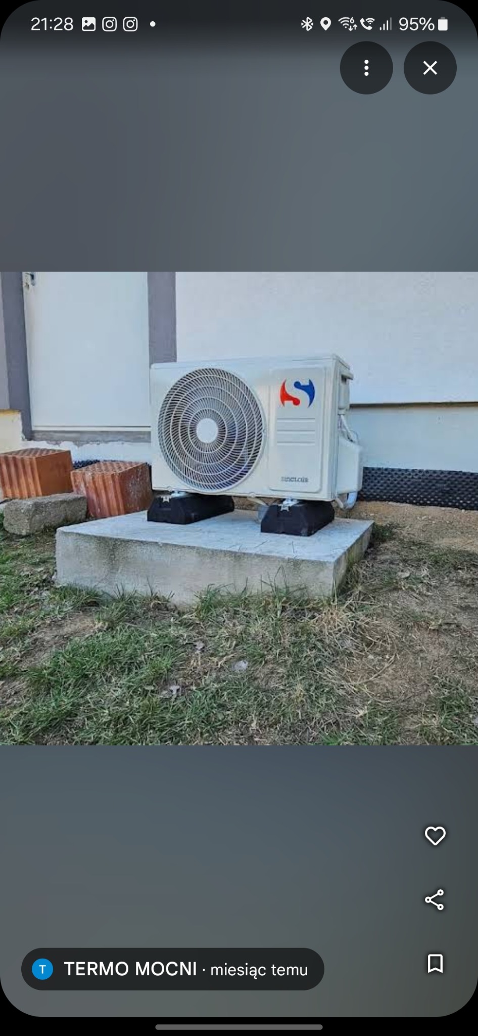 Biała jednostka zewnętrzna klimatyzacji Sinclair zamontowana na betonowym fundamencie, z widocznym logo i fragmentem ściany budynku w tle.