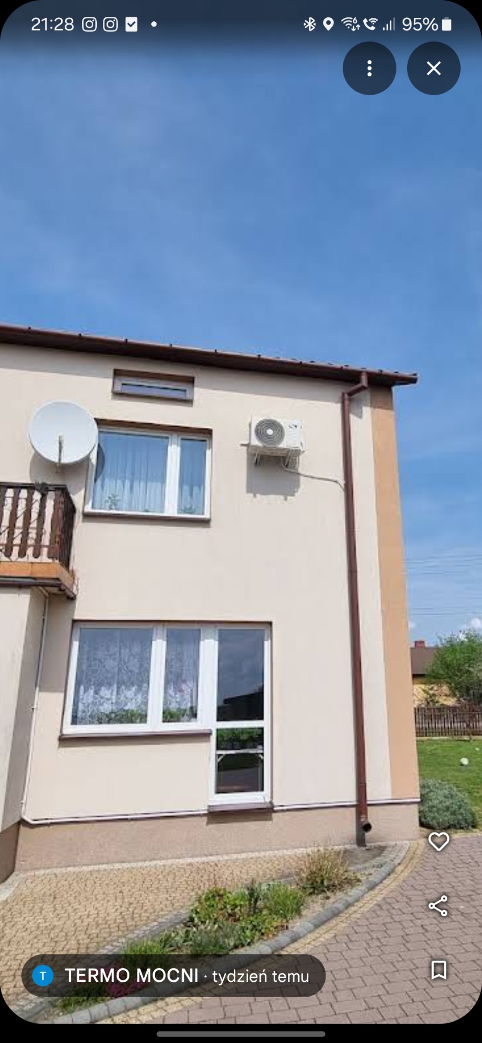 Kremowy dom dwupiętrowy z białymi ramami okiennymi i zamontowaną klimatyzacją na ścianie, widok z zewnątrz w słoneczny dzień.