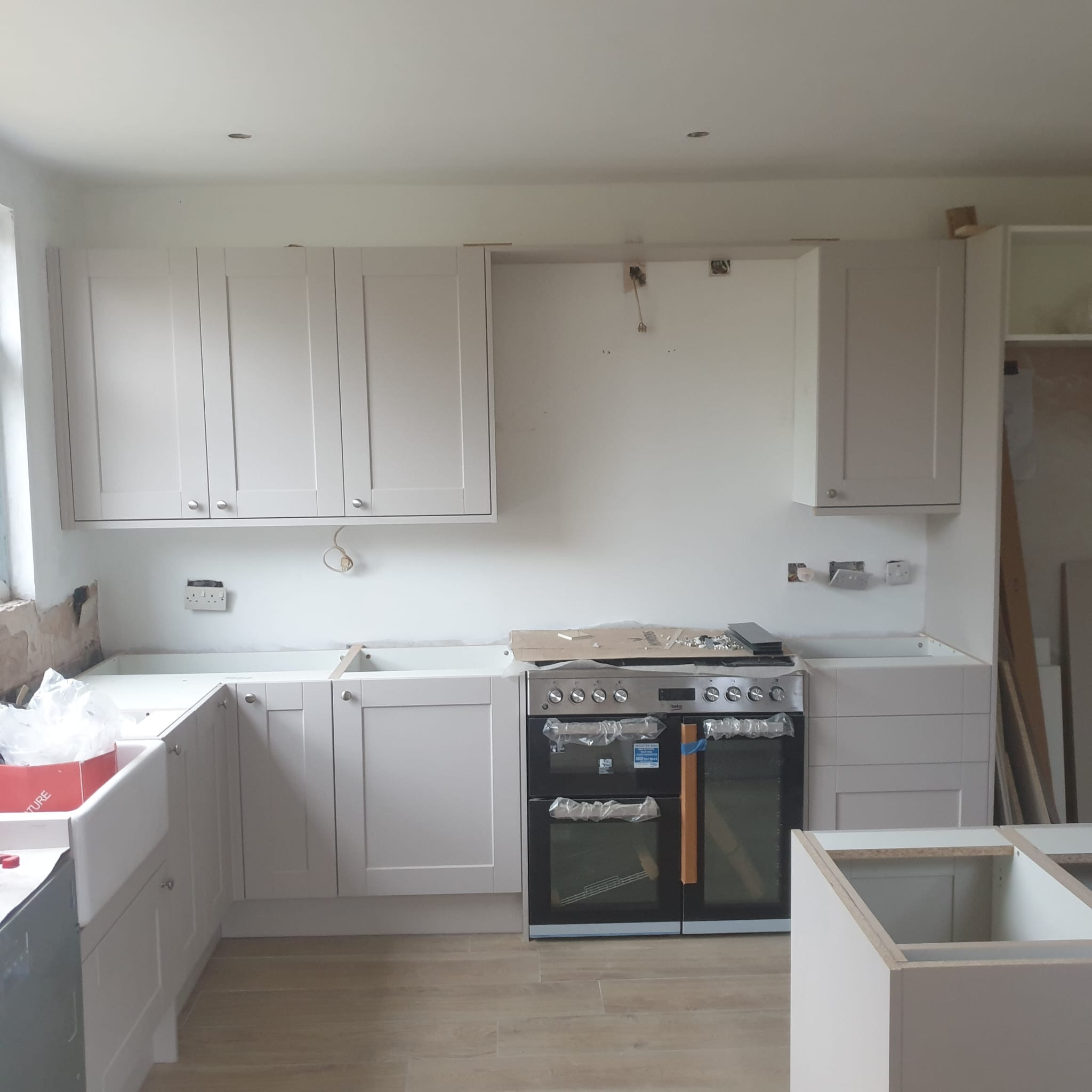 Montaż jasnej kuchni: szafki wiszące i stojące, płyta grzewcza z piekarnikiem. Częściowo widoczne elementy instalacji elektrycznej.