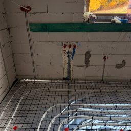 BartSystem Bartosz Kaczmarski - Białe rury ogrzewania podłogowego na folii refleksyjnej, widok z góry, instalacja w surowym stanie, okno z jesiennym widokiem w tle.