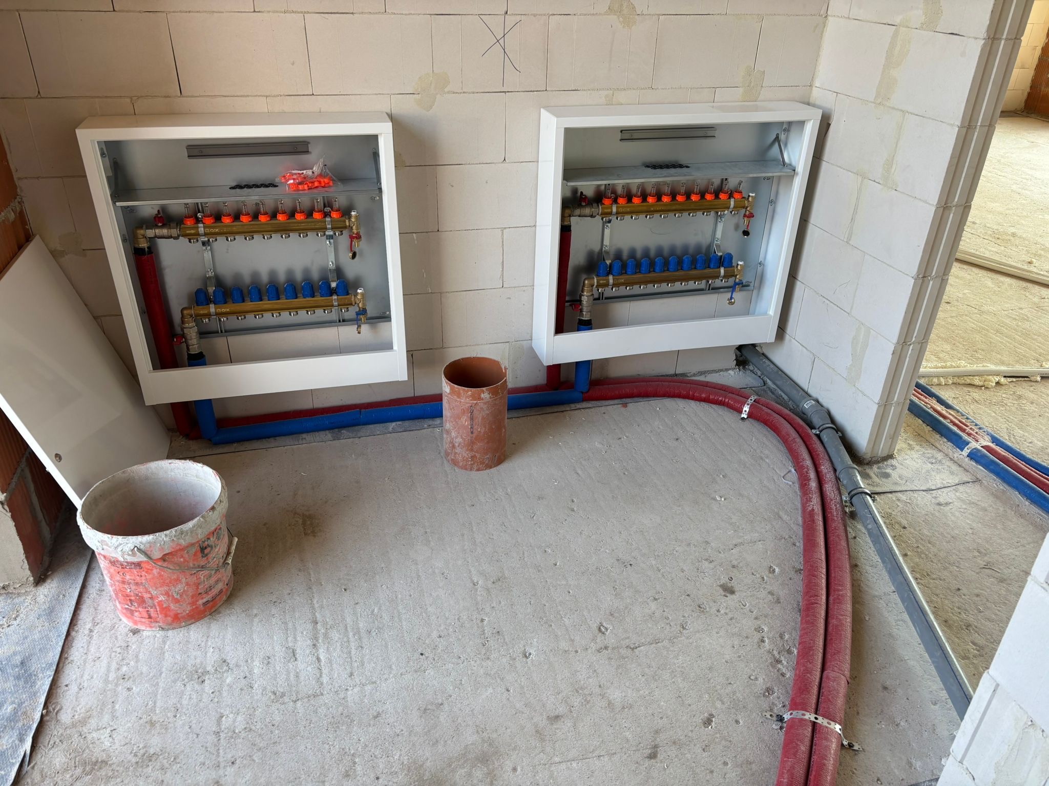 Rozdzielacze ogrzewania podłogowego w skrzynkach, instalacja rur w kolorze czerwonym i niebieskim, widok w trakcie montażu we Wrocławiu.