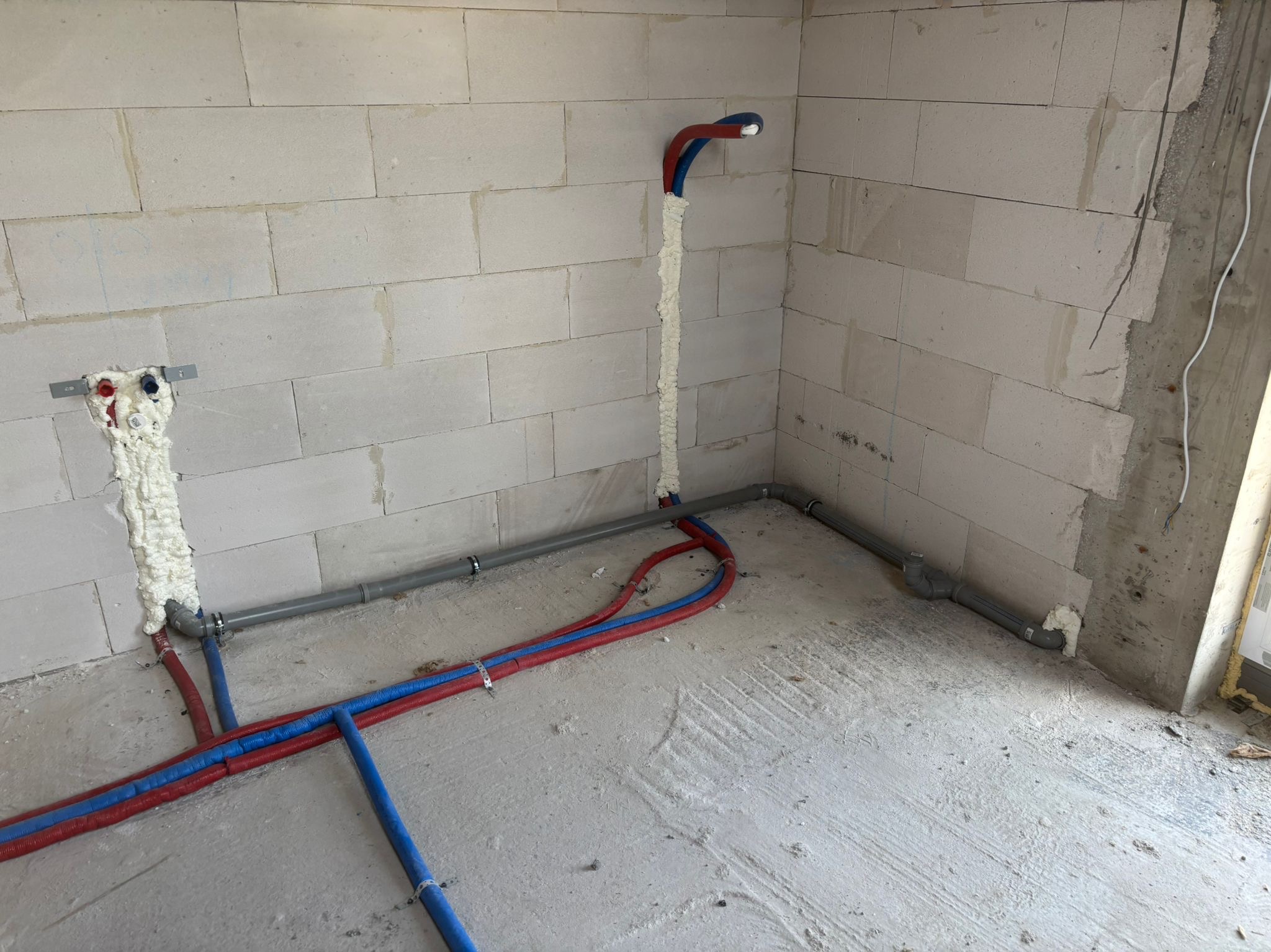 Instalacja rur wodnych i kanalizacyjnych w surowym wnętrzu. Rury grzewcze w izolacji, szare rury kanalizacyjne, pianka montażowa przy ścianach z betonu komórkowego.