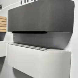 Dwa nowoczesne klimatyzatory ścienne: szary tekstylny i biały, o zaokrąglonych kształtach, zamontowane na białej ścianie. Minimalistyczny design.