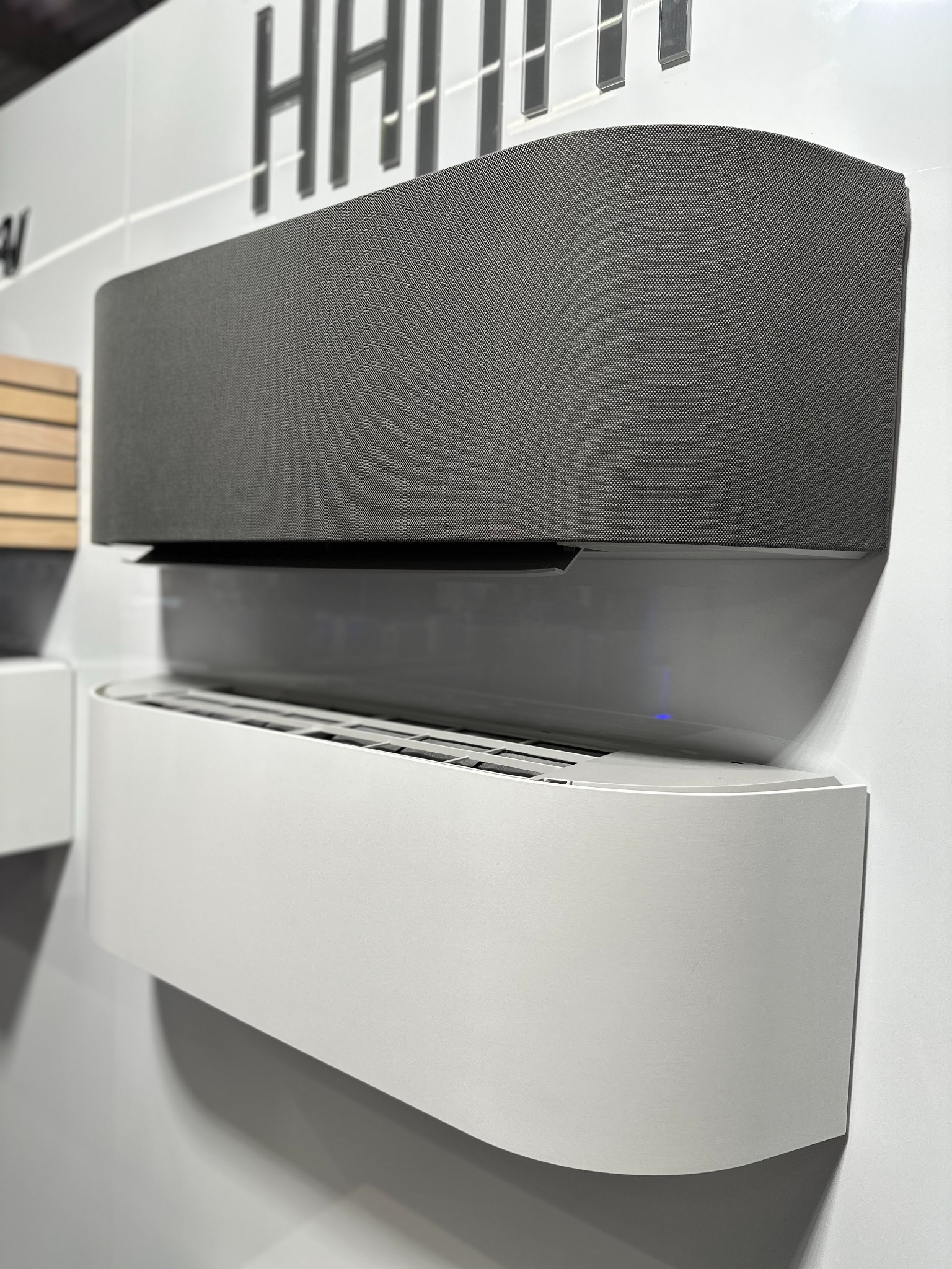 Dwa nowoczesne klimatyzatory ścienne: szary tekstylny i biały, o zaokrąglonych kształtach, zamontowane na białej ścianie. Minimalistyczny design.