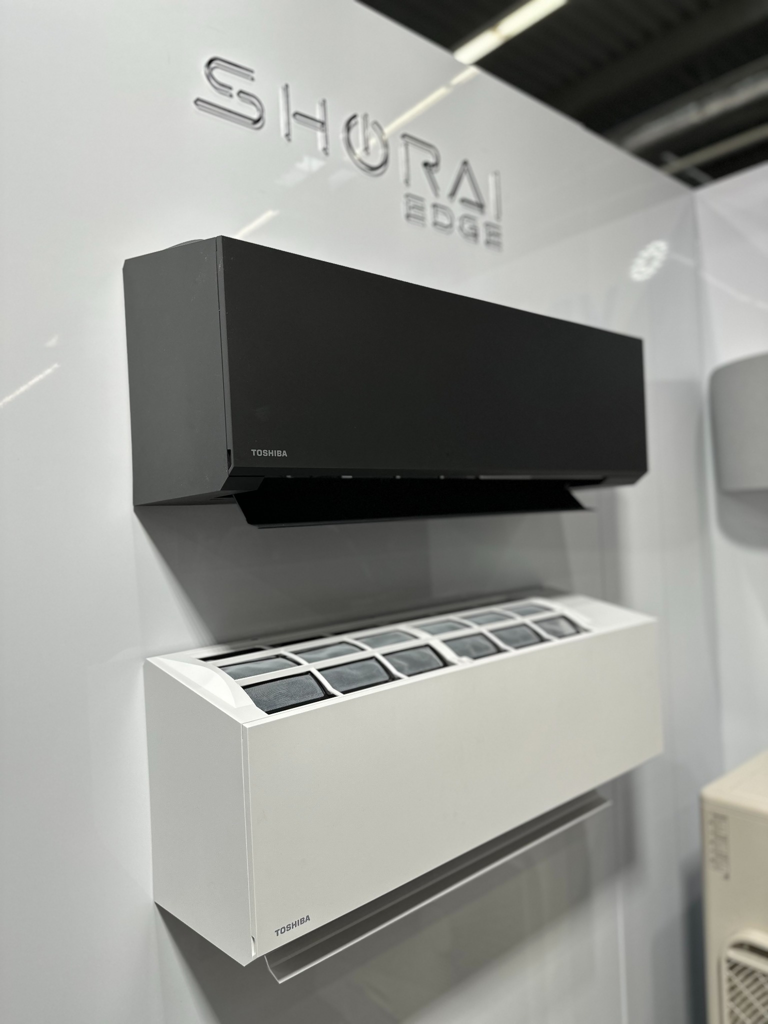 Dwa klimatyzatory Toshiba Shoriai Edge: czarny i biały, zamontowane na ścianie. Widoczny filtr w białym urządzeniu. Minimalistyczny design i nowoczesny wygląd.