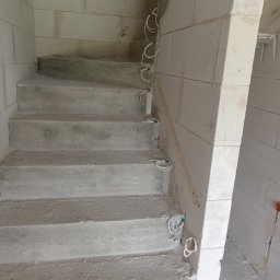 BD ELEKTROHAUS BARTŁOMIEJ DYNIA - Surowe betonowe schody w trakcie budowy z wystającymi przewodami elektrycznymi w ścianie z białych bloczków. Widok z dołu.