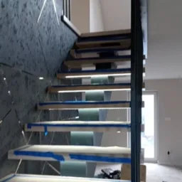 Schody z podświetleniem LED w Osieku Jasielskim, zabezpieczone taśmą malarską, z nowoczesną balustradą i dekoracyjną ścianą. Widok z dołu.