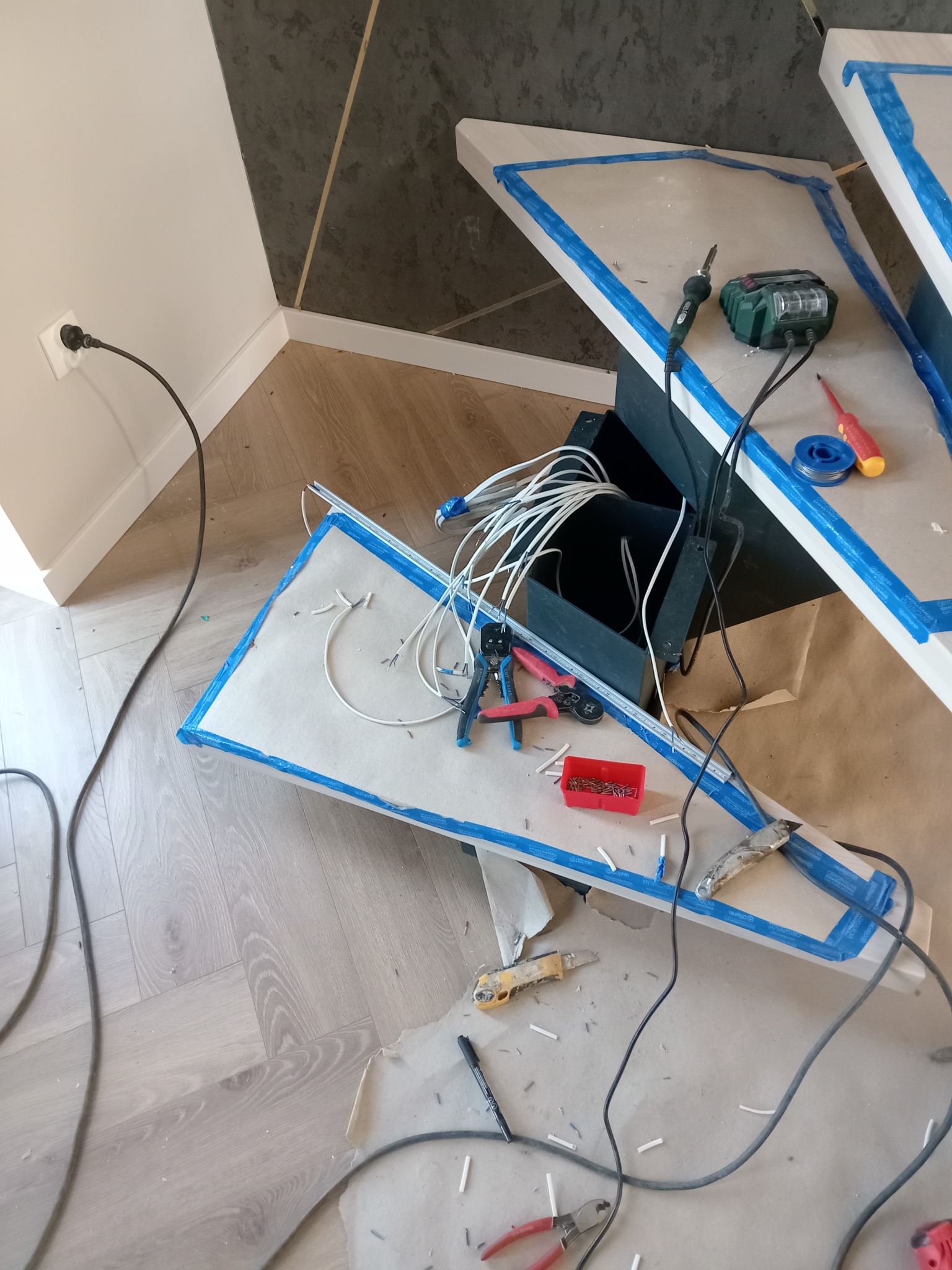 Przygotowanie do montażu oświetlenia: przewody, narzędzia (lutownica, wkrętak) i elementy mocujące na zabezpieczonej powierzchni. Widoczne gniazdko elektryczne.