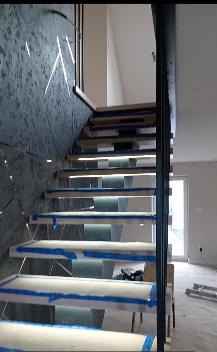 Schody z podświetleniem LED w Osieku Jasielskim, zabezpieczone taśmą malarską, z nowoczesną balustradą i dekoracyjną ścianą. Widok z dołu.