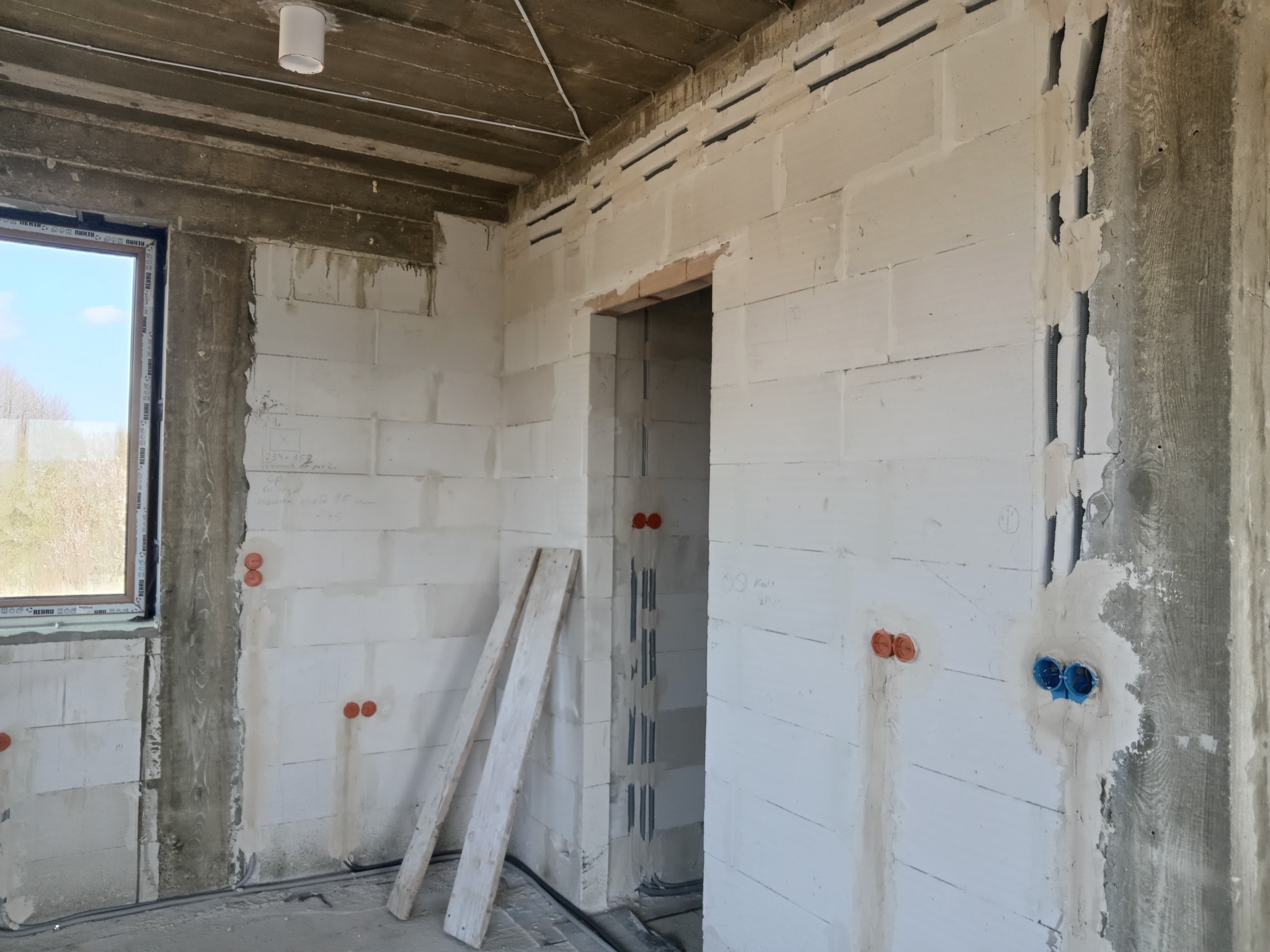 Wnętrze w stanie surowym z widocznymi instalacjami elektrycznymi w ścianach z betonu komórkowego. Widoczne puszki instalacyjne i bruzdy pod kable.