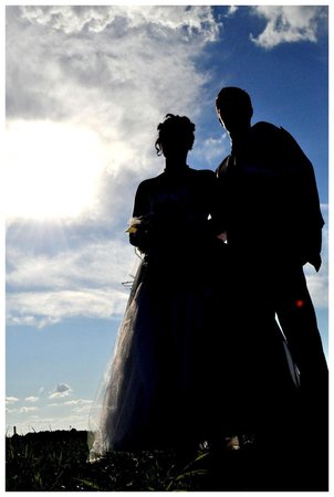Sylwetki pary młodej na tle błękitnego nieba z chmurami i słońcem, widok z dołu.