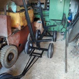 Skrawmet-plast - Metalowa konstrukcja na kołach, z pionowymi wspornikami, na tle warsztatu z maszynami. Widoczne elementy konstrukcyjne i spawane łączenia.